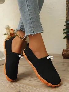 Atmungsaktive schwarze Barfußschuhe aus Strick mit orangefarbener Sohle am Modell.