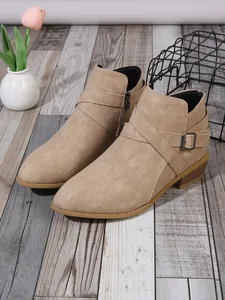 Close-up detail of beige suede pointed toe Chelsea boots with criss-cross buckle straps