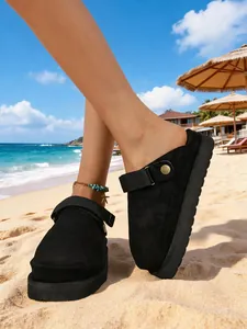 Gros plan de sabots plateforme en daim noir pour femmes sur une plage ensoleillée