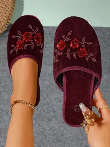 Primo piano di pantofole in velluto rosso vino con paillettes e ricami floreali.