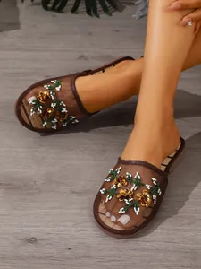 Detailed view of the sequined floral embroidery on brown mesh flat mule slippers.