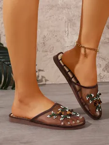 Detailed view of elegant coffee mesh mules featuring floral bead embroidery on model's feet.