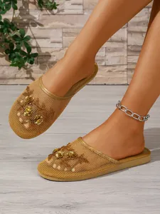 Nahaufnahme goldener Mesh-Pantoletten mit feiner Blumenstickerei und Goldpailletten.