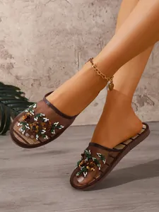 Close-up of brown mesh mule slippers with floral embroidery and sequins on a model.