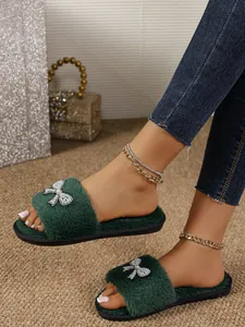 Dettaglio ravvicinato delle pantofole in peluche verde con fiocco in perle e strass.