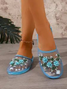 Elegant light blue mesh mule slippers with delicate 3D floral embroidery on model feet.