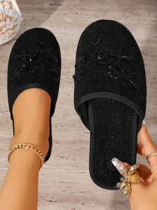 Dettaglio ravvicinato di pantofole in velluto nero con eleganti applicazioni floreali e perline.