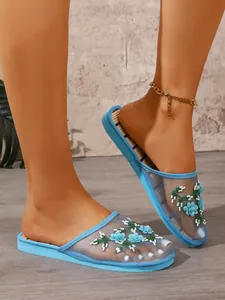 Detail of elegant floral embroidery on light blue mesh flat mule slippers for home.