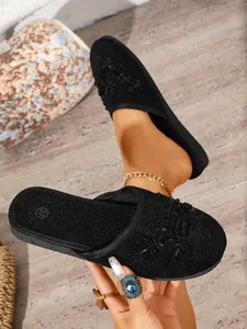 Primo piano di pantofole in camoscio nero a punta chiusa con eleganti applicazioni floreali.
