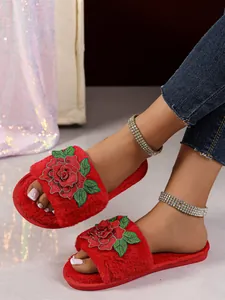 Dettaglio delle pantofole in peluche rosso con ricamo di rosa e consistenza morbida.