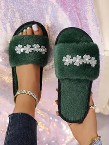 Primo piano di ciabatte in ecopelliccia verde scuro con eleganti fiori di perle e strass.