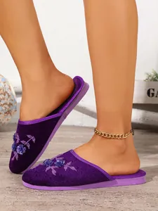 Dettaglio di pantofole da casa in velluto viola con elegante ricamo floreale e paillettes
