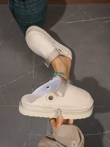 Gros plan de sabots à plateforme beige avec texture en daim et boucle métallique.