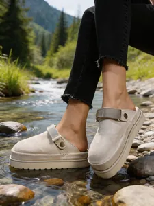 Gros plan de mules à plateforme en daim beige portées près d'un ruisseau naturel
