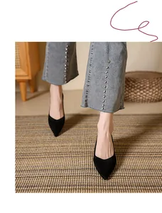 Close-up view of black suede pointed-toe pumps worn with denim jeans on a rug.