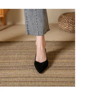 Close-up front view of black suede pointed-toe pump shoes on a woven rug background.