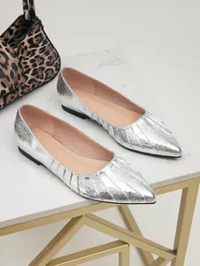 Gros plan de ballerines argentées plissées à bout pointu élégantes sur surface en marbre