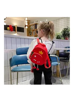 Vista trasera de una niña con una mochila roja de dinosaurio de dibujos en una cafetería