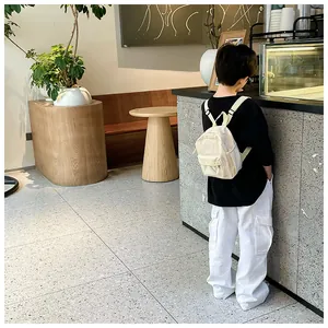 Vue de dos d'un enfant portant un mini sac à dos crème élégant dans un café moderne