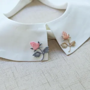 Detailed macro shot of delicate pink rose embroidery patches on a white collar