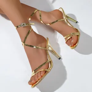 Detail view of gold strappy stiletto sandals featuring rhinestone buckle on feet.