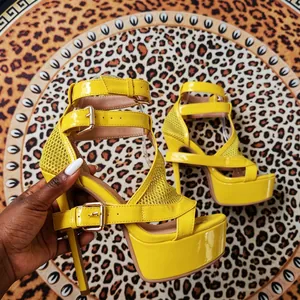 Detailansicht gelber Plateau-Sandalen aus Lackleder mit Goldschnallen und Mesh.