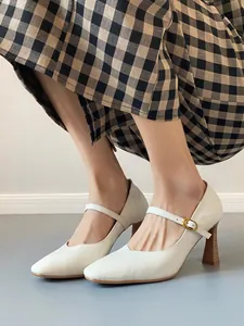 Close-up of white leather Mary Jane heels with wooden block heel and gold buckle detail