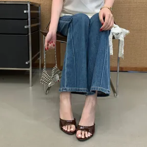 Brown patent leather high-heel mules with round toe, styled with denim jeans.