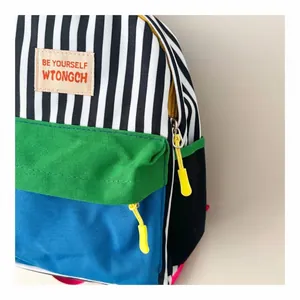 Dettaglio di uno zaino per bambini a righe colorate con una toppa 'Be Yourself'.