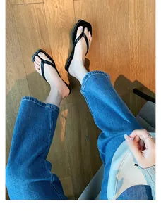 Stylische Frau trägt schwarze Leder-Zehentrenner mit quadratischer Spitze und blauen Jeans