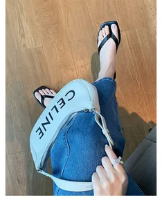Nahaufnahme einer weißen Lederhandtasche und schwarzer Flip-Flops an einem Model in Jeans