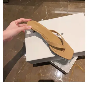 Nahaufnahme von khakifarbenen Leder-Flip-Flop-Sandalen mit Absatz in der Hand