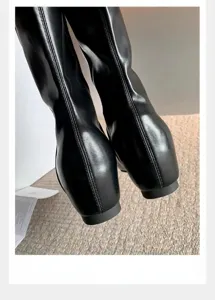 Vista trasera detallada de botines minimalistas de cuero negro con cuña oculta de 5 cm