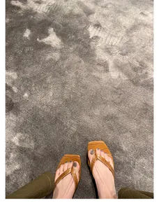 Detailansicht brauner Leder-Flip-Flops mit Krokoprägung auf grauem Teppichboden