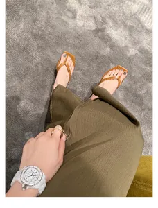 Detailansicht brauner flacher Leder-Flip-Flops an einem Model mit olivgrünem Rock