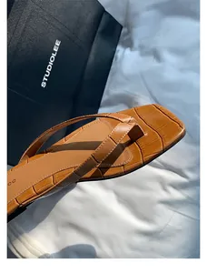 Nahaufnahme von eleganten braunen Leder-Flip-Flops mit Krokomuster und feiner Naht.