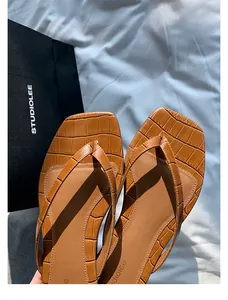 Nahaufnahme brauner Leder-Flip-Flops mit Krokodilmuster und Markenlogo studiolee