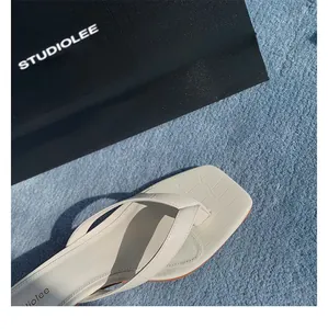 Nahaufnahme der cremefarbenen Leder-Flip-Flops mit Krokoprägung und eckiger Zehenpartie