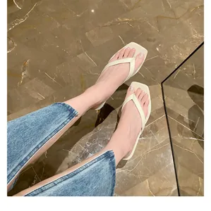 Nahaufnahme von oben: Eine Frau trägt weiße Leder-Flip-Flops mit quadratischer Zehenpartie