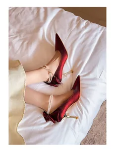 Primer plano de zapatos de novia en satén rojo con pulsera de perlas y lazo elegante