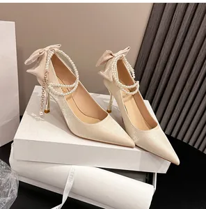 Primer plano de elegantes zapatos de novia en raso champán con cadena de perlas y lazo