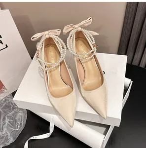 Primer plano de tacones de novia en satén champán con cadena de perlas y lazo.