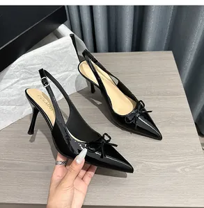 Primo piano di eleganti décolleté slingback in vernice nera con dettaglio a fiocco.