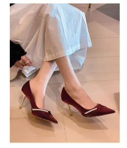 Primer plano de elegantes tacones burdeos con cadena de perlas y tacón de aguja.