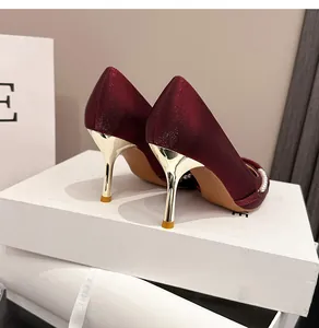 Elegantes tacones de satén granate con tacón de aguja dorado y una cadena de perlas
