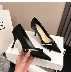 Vista detallada de zapatos negros de tacón con cadena de perlas y lazo decorativo.