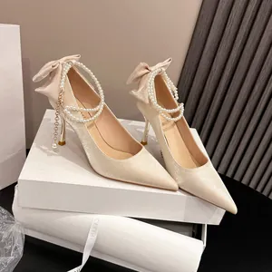 Elegantes zapatos de novia de raso champán con una cadena de perlas y un lazo muy decorativo.
