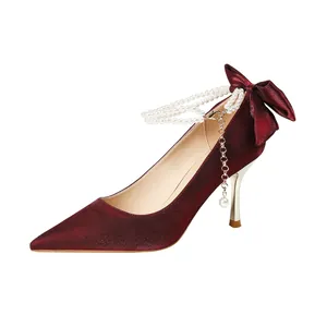 Elegantes tacones de satén burdeos con correa de perlas al tobillo y lazo decorativo.