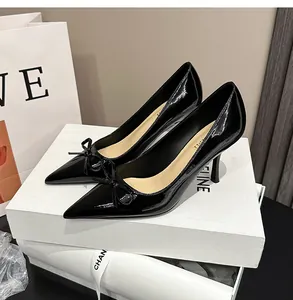 Schwarze Lackleder-Stilettos mit spitzer Kappe und Schleife auf weißen Schachteln.