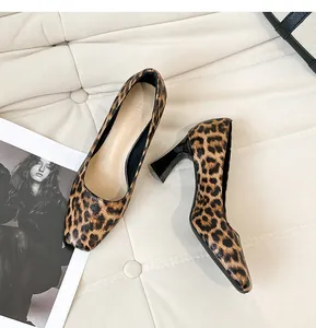 Close-up of leopard print pumps with square toe and black flare heels on beige